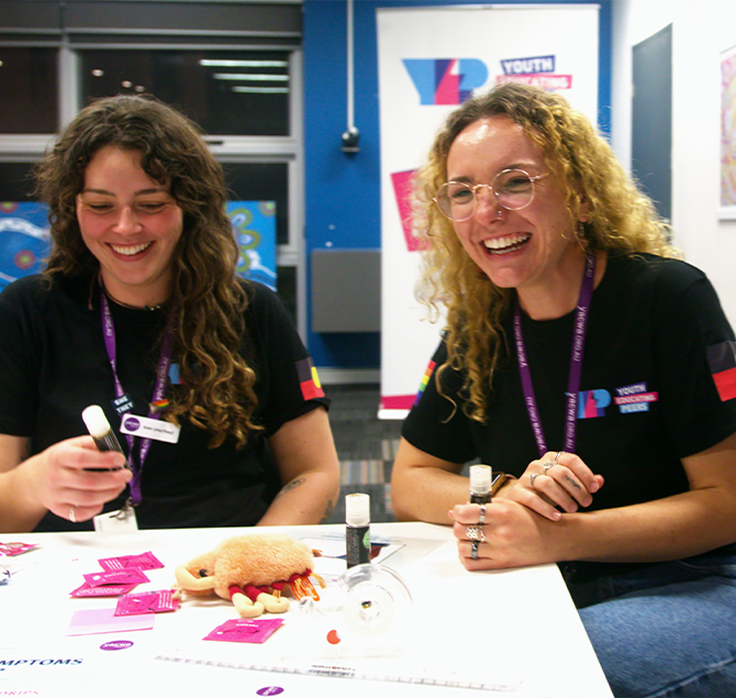 Two YEP crew members facing the camera and laughing, surrounded by sexual health education materials